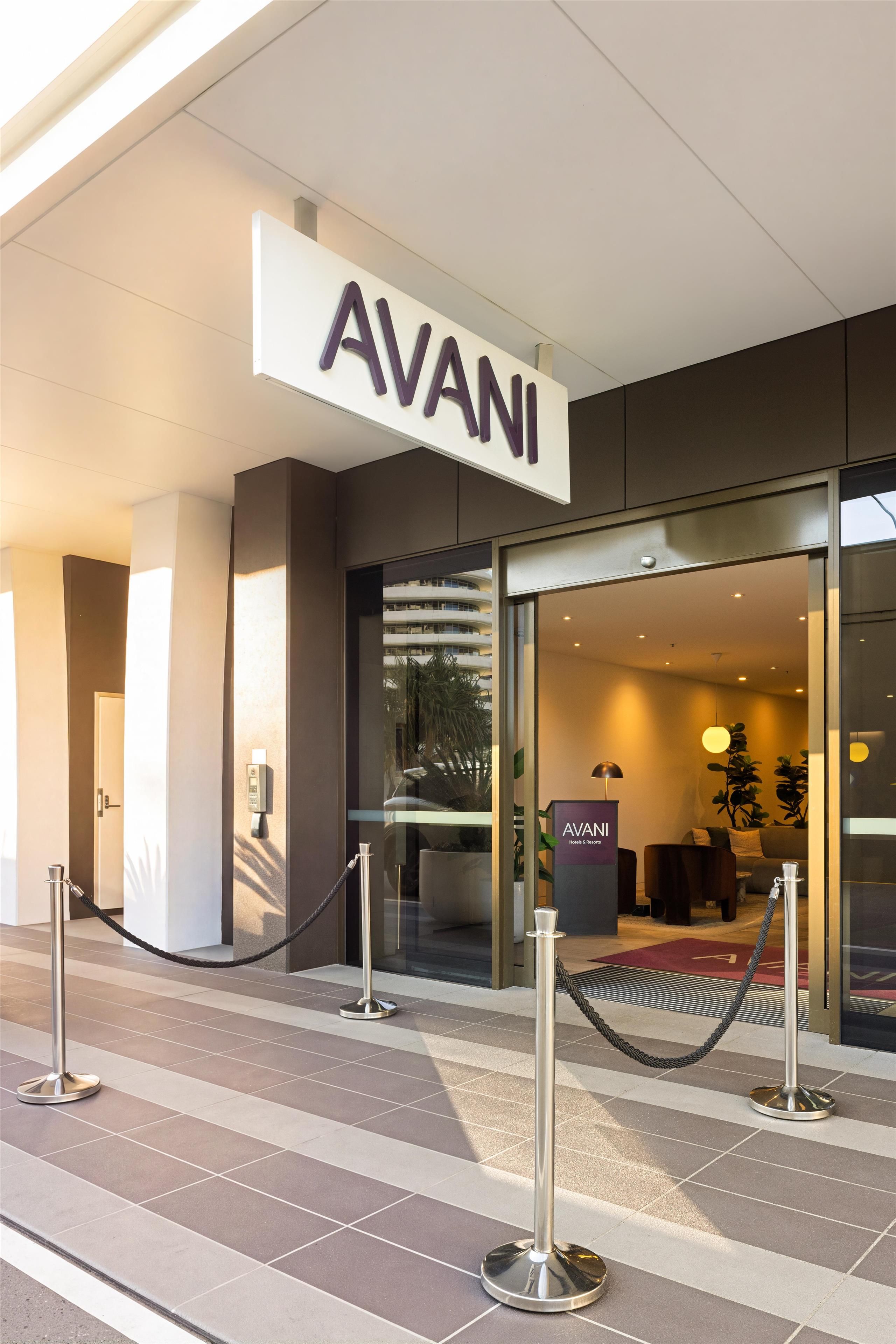 The exterior of a hotel with a prominent 'AVANI' sign, a glass entrance, and a reception desk inside.