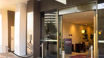 The exterior of a hotel with a prominent 'AVANI' sign, a glass entrance, and a reception desk inside.