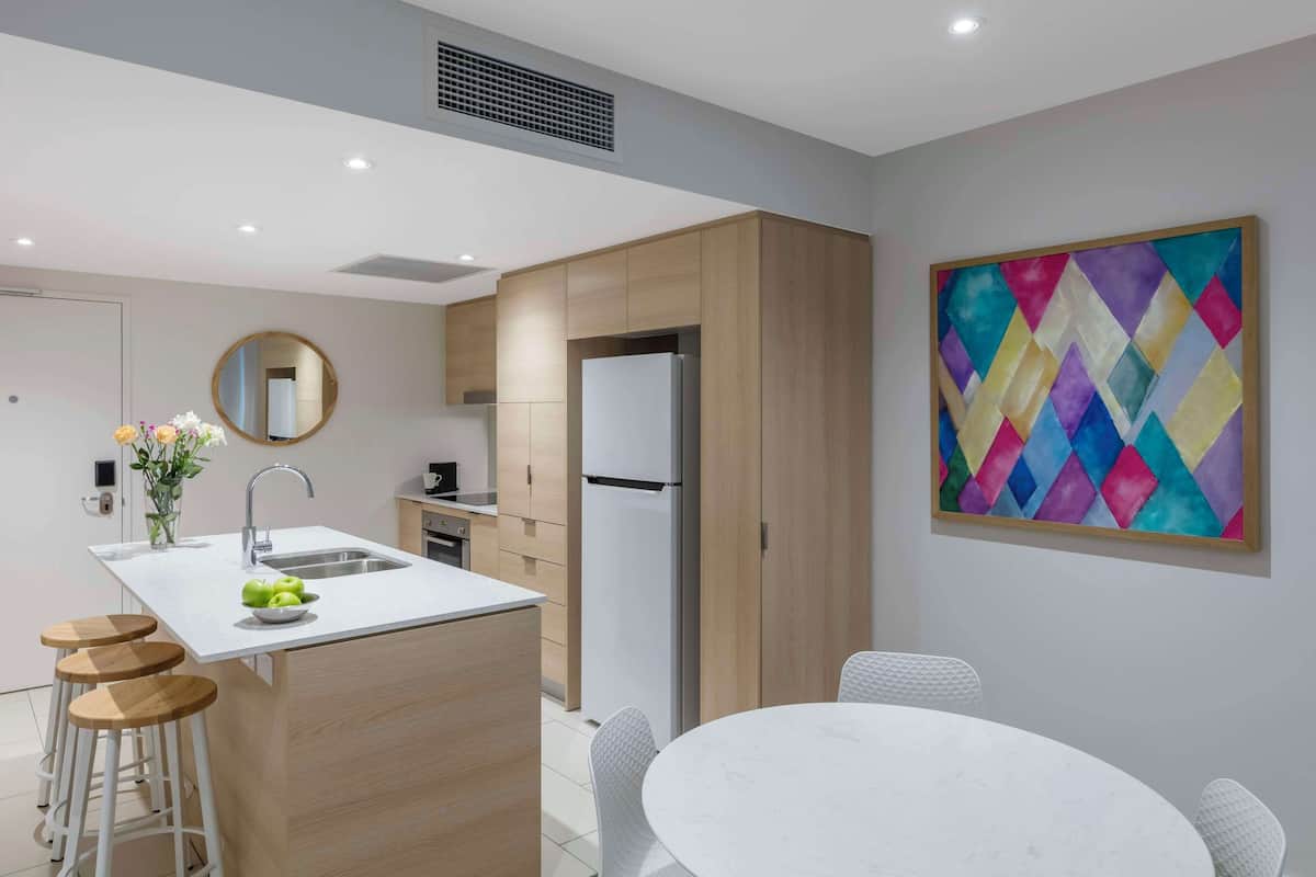 A modern kitchen with a central island, wooden cabinets, a refrigerator, and a dining area with a white table and chairs.