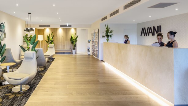 Una zona de recepción con suelo de madera, sillas modernas, un mostrador de recepción y un cartel en la pared.