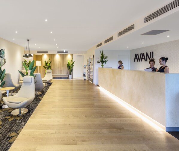 A reception area with a wooden floor, modern chairs, a reception desk, and a wall-mounted sign. - Avani Broadbeach Residences (Broadbeach)