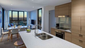 A modern kitchen with a large island, stainless steel appliances, and a view of the city. - Avani Broadbeach Residences (Broadbeach)