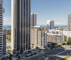 A high-rise building with multiple floors, a prominent 'AVANI' sign at the base, and a view of the ocean in the background. - Avani Broadbeach Residences (Broadbeach)