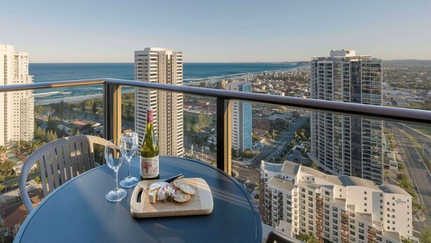 A balcony with a table set for a meal, overlooking a cityscape and the sea. - Avani Broadbeach Residences (Broadbeach)