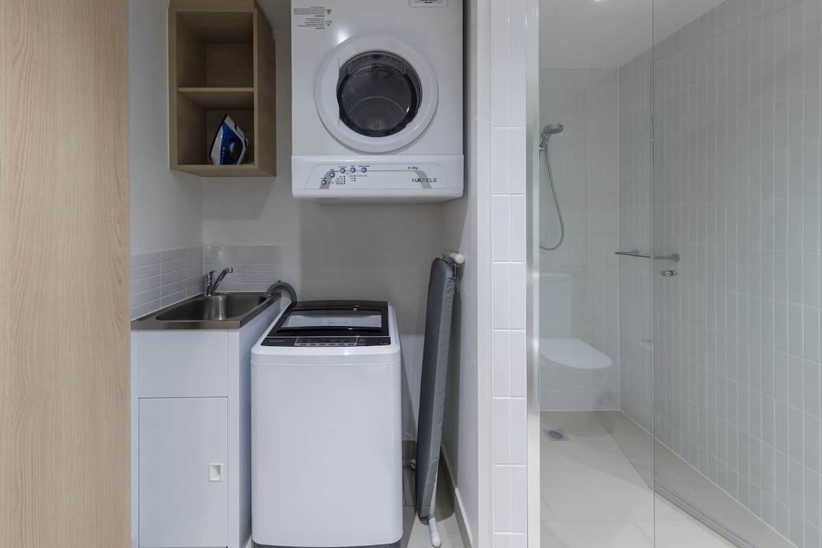 A compact laundry room with a washing machine, a dryer, and a shower area.