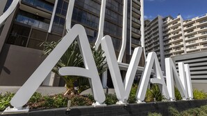 A modern building with large white letters spelling "AVANI" in the foreground, surrounded by greenery and a clear sky. - Avani Broadbeach Residences (Broadbeach)