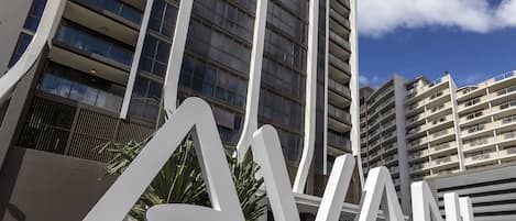 Un bâtiment moderne, avec de grandes lettres blanches formant le mot « AVANI » au premier plan, entouré de verdure et sous un ciel dégagé.