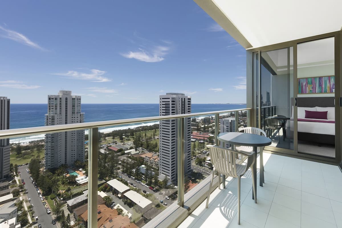 A balcony with a view of the ocean and cityscape, a small table, and a chair.