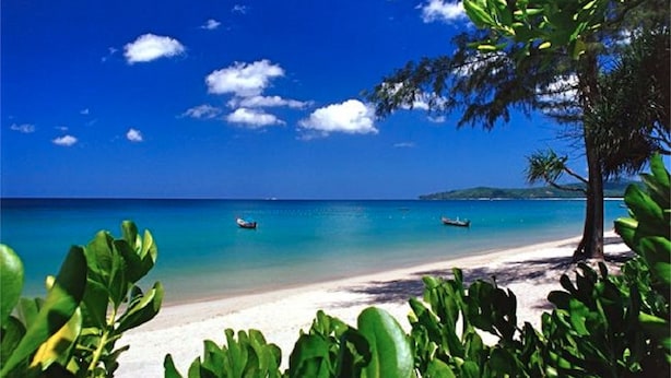 Ein Strand mit klarem türkisfarbenem Wasser, einem sandigen Ufer und einigen Booten.
