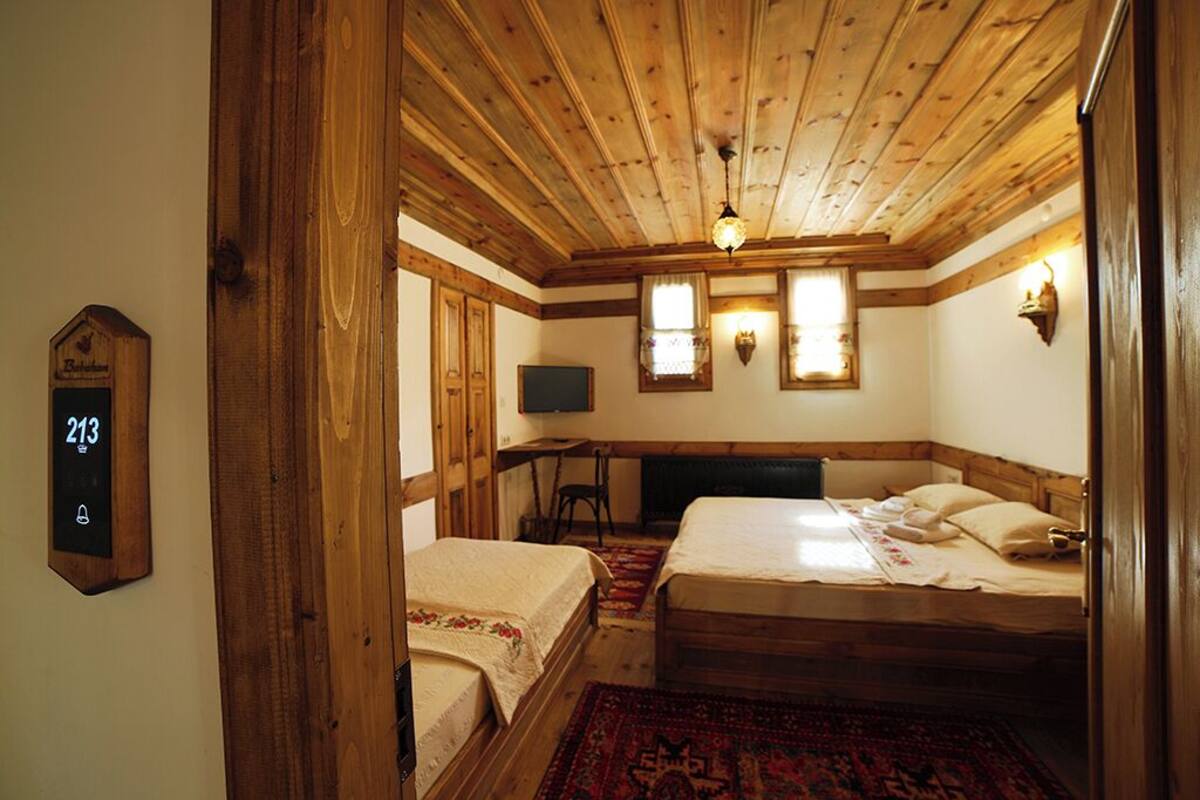 Een kamer met houten balkenplafond, twee bedden, een bureau en een klok aan de muur.