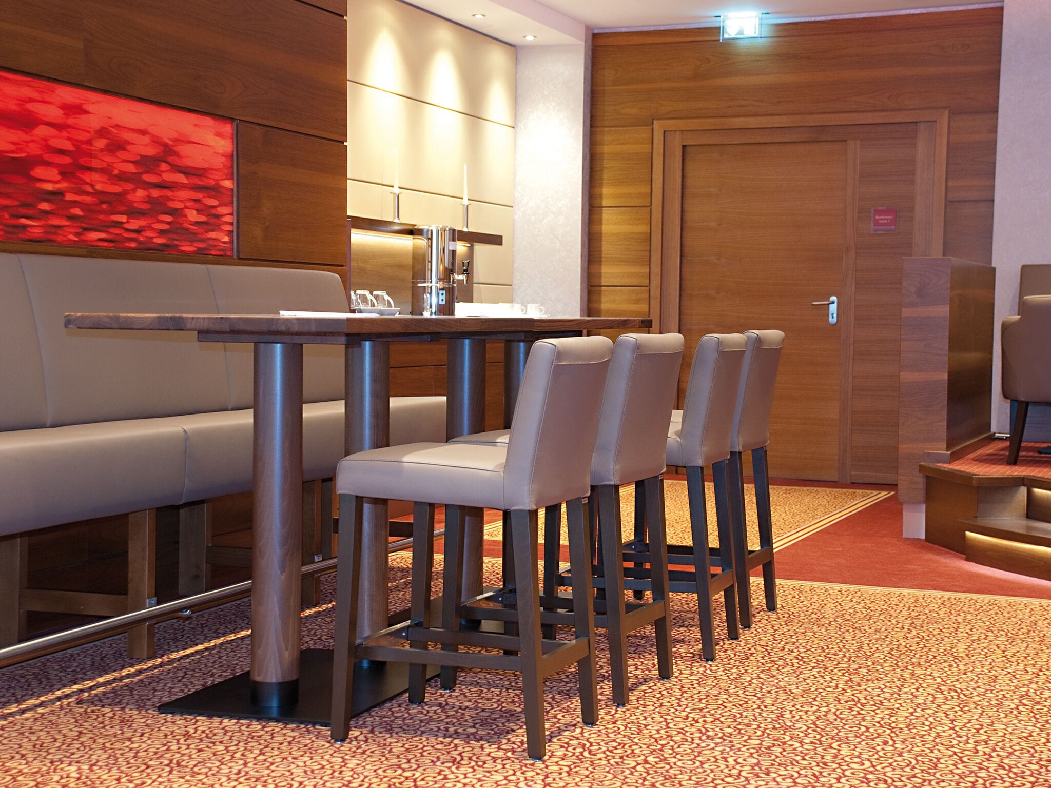 Un comedor de hotel moderno con una mesa larga, cuatro taburetes de bar y un sofá.