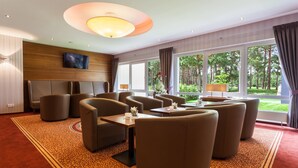 A hotel room with a large window, a flat-screen TV, and a seating area with sofas and a table. - Morada Hotel Heidesee Gifhorn (Gifhorn)
