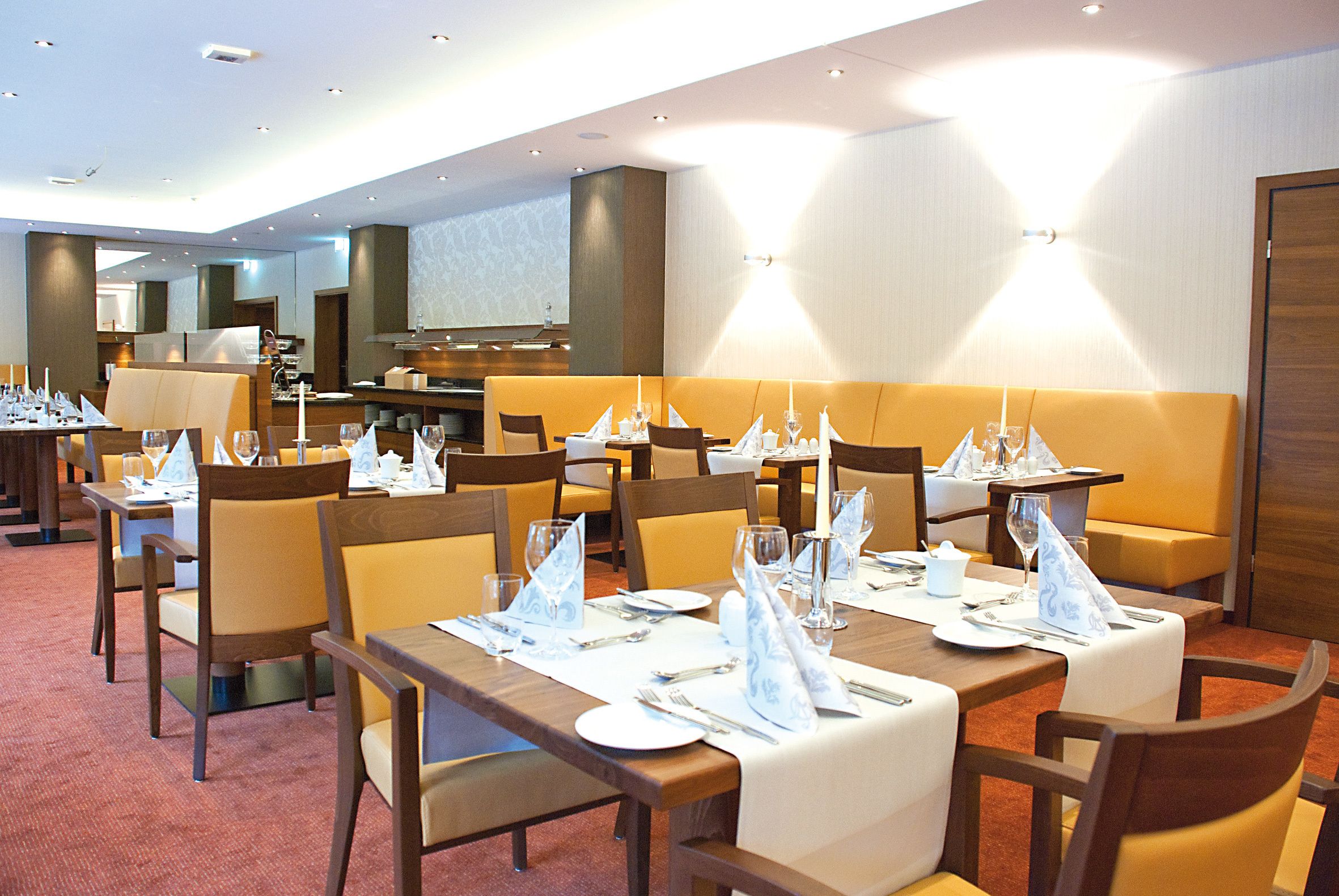 Un comedor de hotel con varias mesas dispuestas para los huéspedes, equipado con manteles, servilletas y cubiertos.