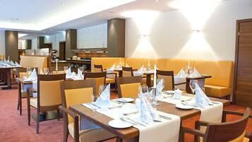 Un comedor de hotel con varias mesas dispuestas para los huéspedes, equipado con manteles, servilletas y cubiertos.