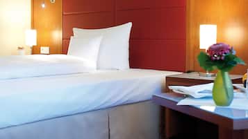 A hotel room with a bed, bedside table, and a vase with flowers.