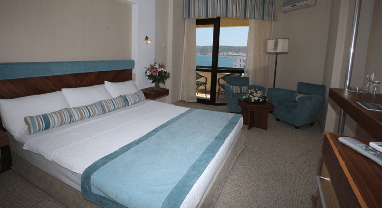 A hotel room with a large bed, a balcony with a view, a desk, and a chair.