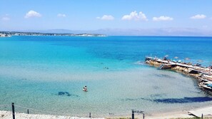 A coastal view with clear turquoise waters, a pier with umbrellas, and a rocky shoreline. - Babaylon Hotel (Cesme)