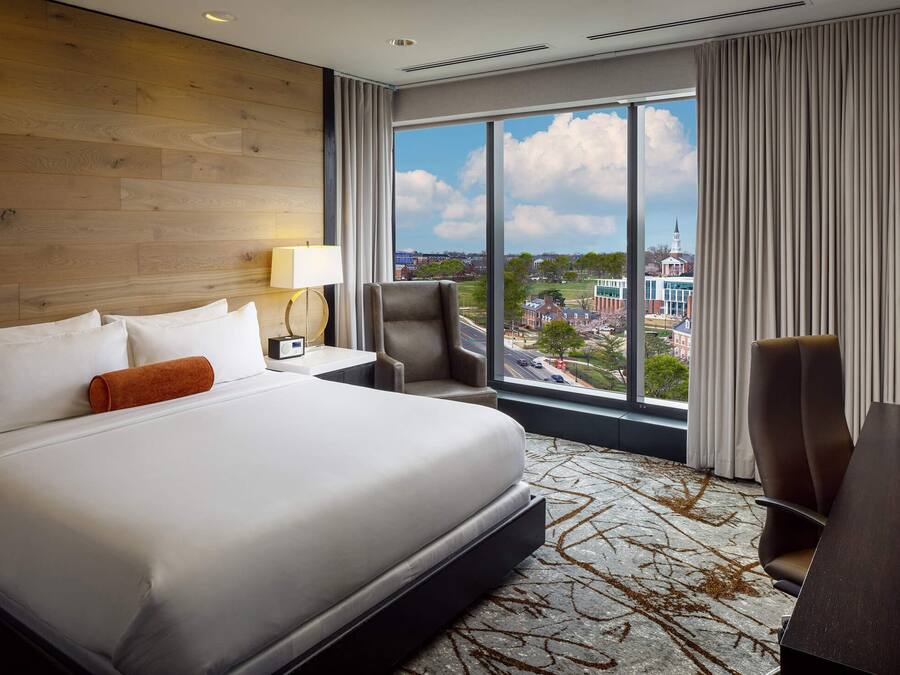 A hotel room with a large bed, a desk, a chair, and a TV.