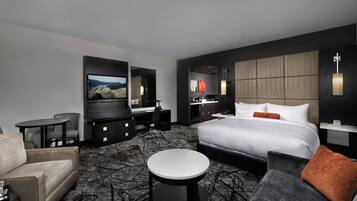 A modern hotel room with a large bed, a desk, a TV, and a seating area.