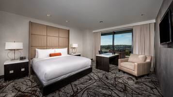 Quarto de hotel com uma cama grande, uma escrivaninha, uma cadeira e uma televisão.