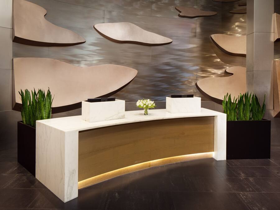 A reception desk with a marble top and a wooden base, flanked by two black planters with green plants.