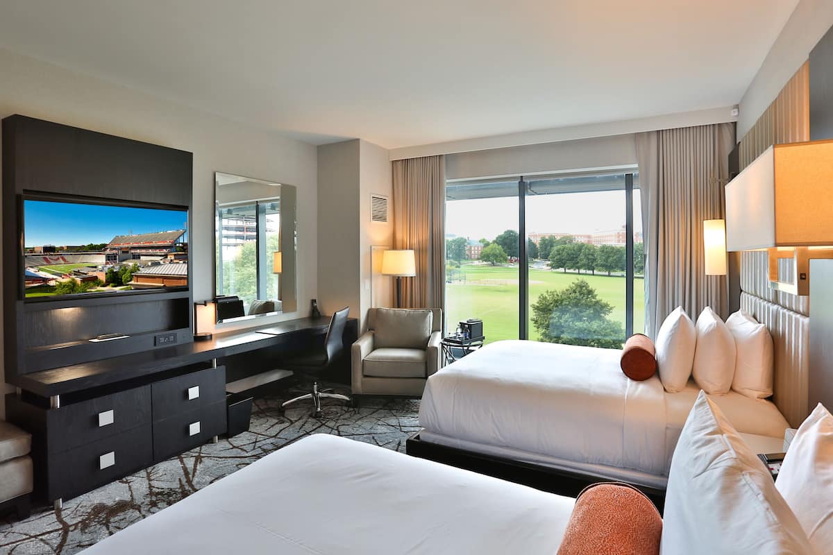 A hotel room with a large bed, a desk with a TV, a chair, and a view of a golf course.