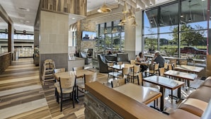 Un restaurante moderno con suelo de madera, ventanas amplias y una variedad de opciones de asientos, incluyendo mesas y cabinas.