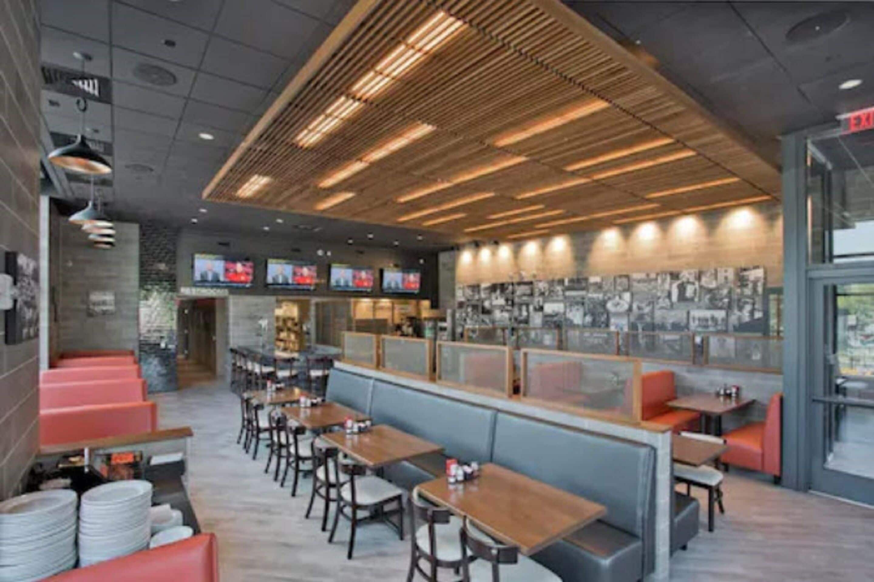 Un interior de restaurante moderno con paneles de techo de madera, zonas de estar y una pared de cuadros enmarcados.