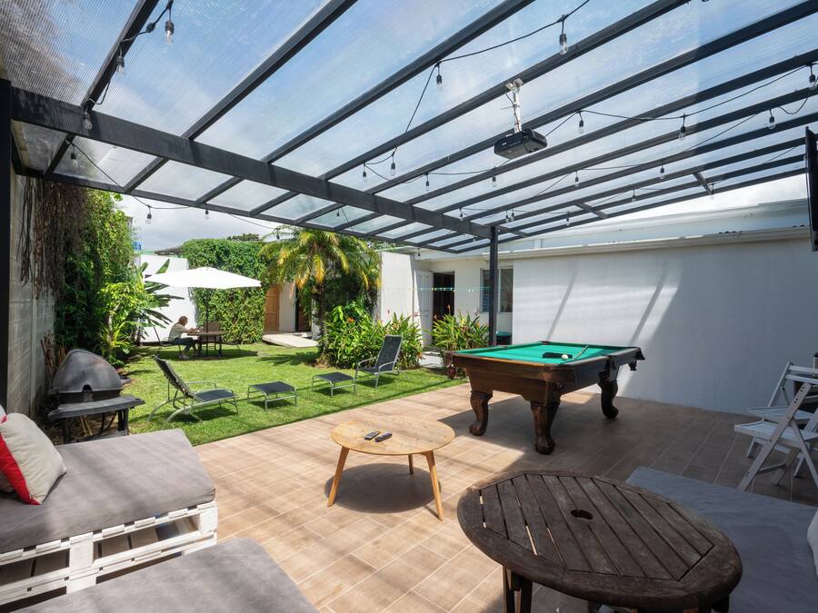 Eine überdachte Terrasse im Freien mit Billardtisch, Liegestühlen und Grill.