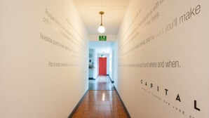 A hallway with a wooden floor and white walls with text. There is a red door at the end of the hallway. - Capital Hostel de Ciudad (San José)