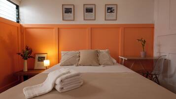 A hotel room with a large bed, a bedside table with a lamp, a chair, and a small table with a plant.