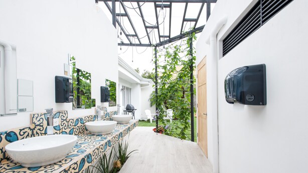A modern bathroom with a large white sink, a patterned tile backsplash, and a small garden area with a pergola. - Capital Hostel de Ciudad (San José)
