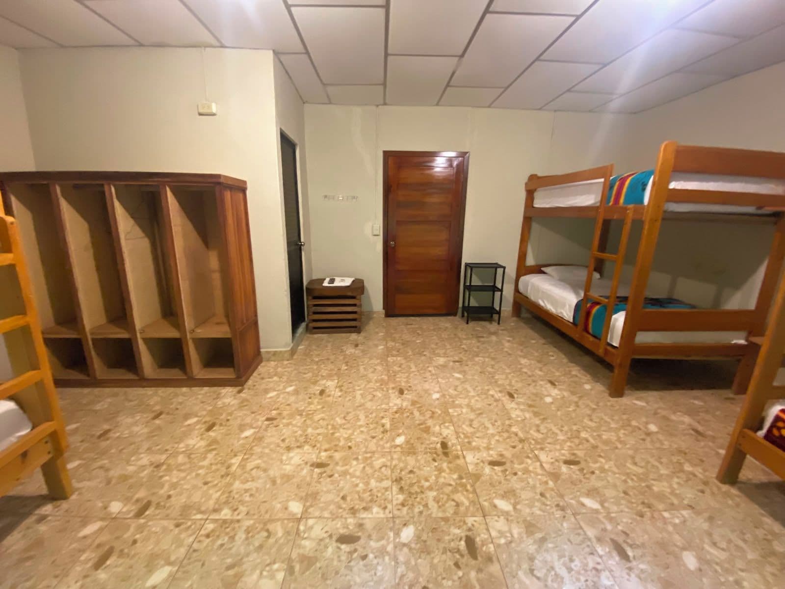 A room with a wooden wardrobe, bunk beds, a small stool, and a door.