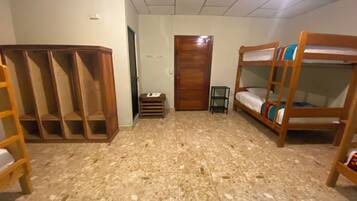 A room with a wooden wardrobe, bunk beds, a small stool, and a door.