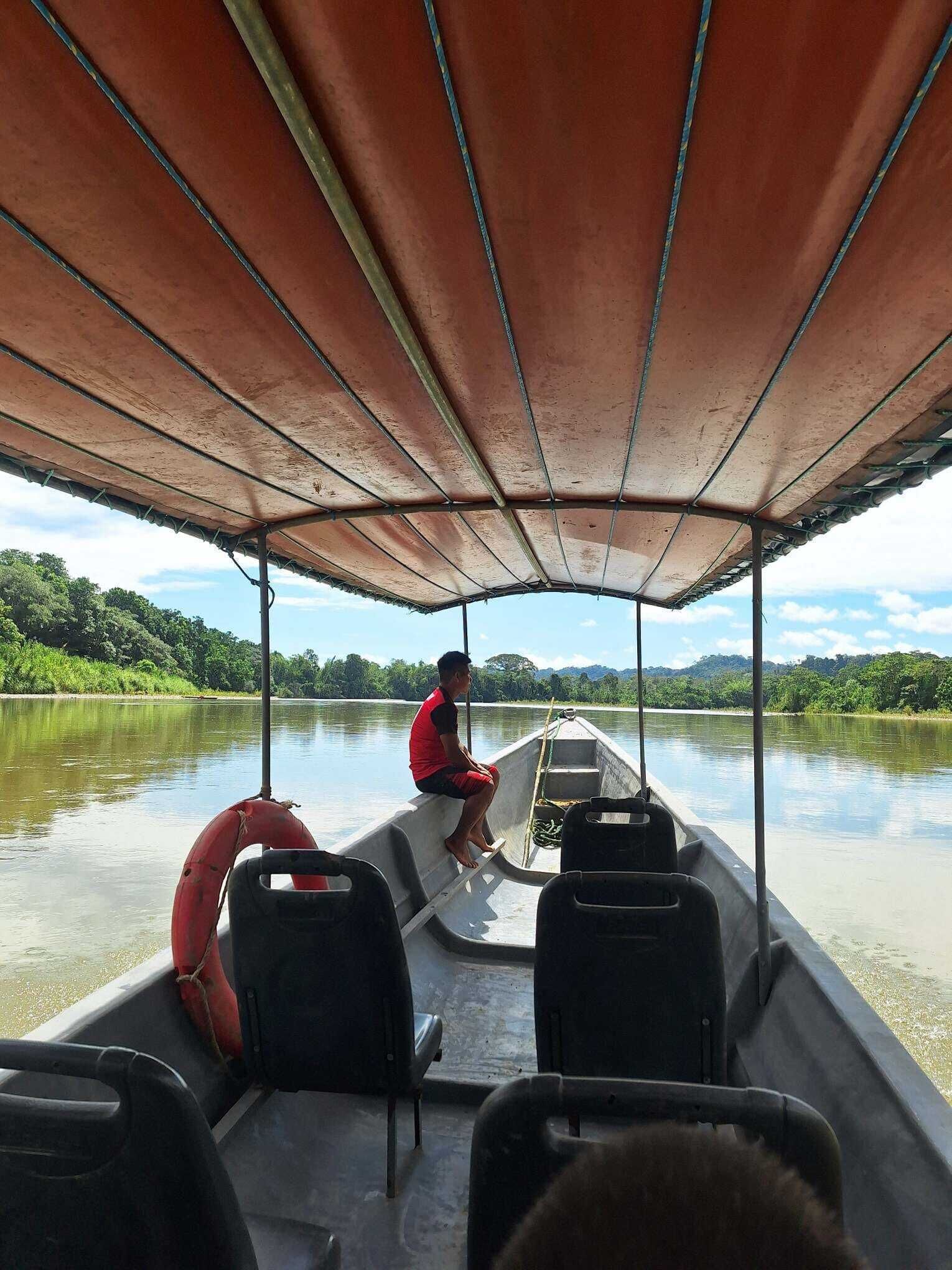A boat with a covered deck, a person sitting at the front, and calm water in the background.