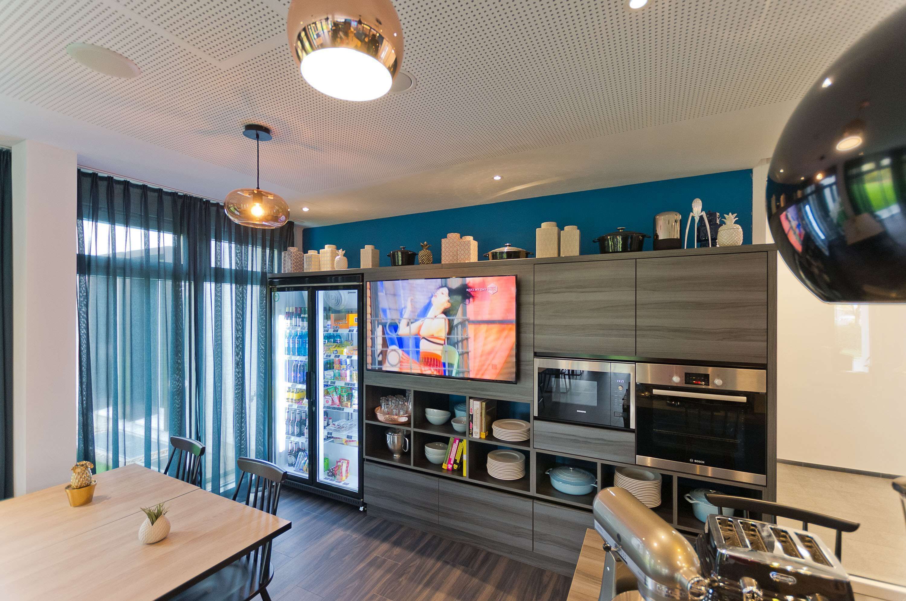 A modern kitchen with a flat-screen TV, stainless steel appliances, and a dining area with a wooden table and chairs.
