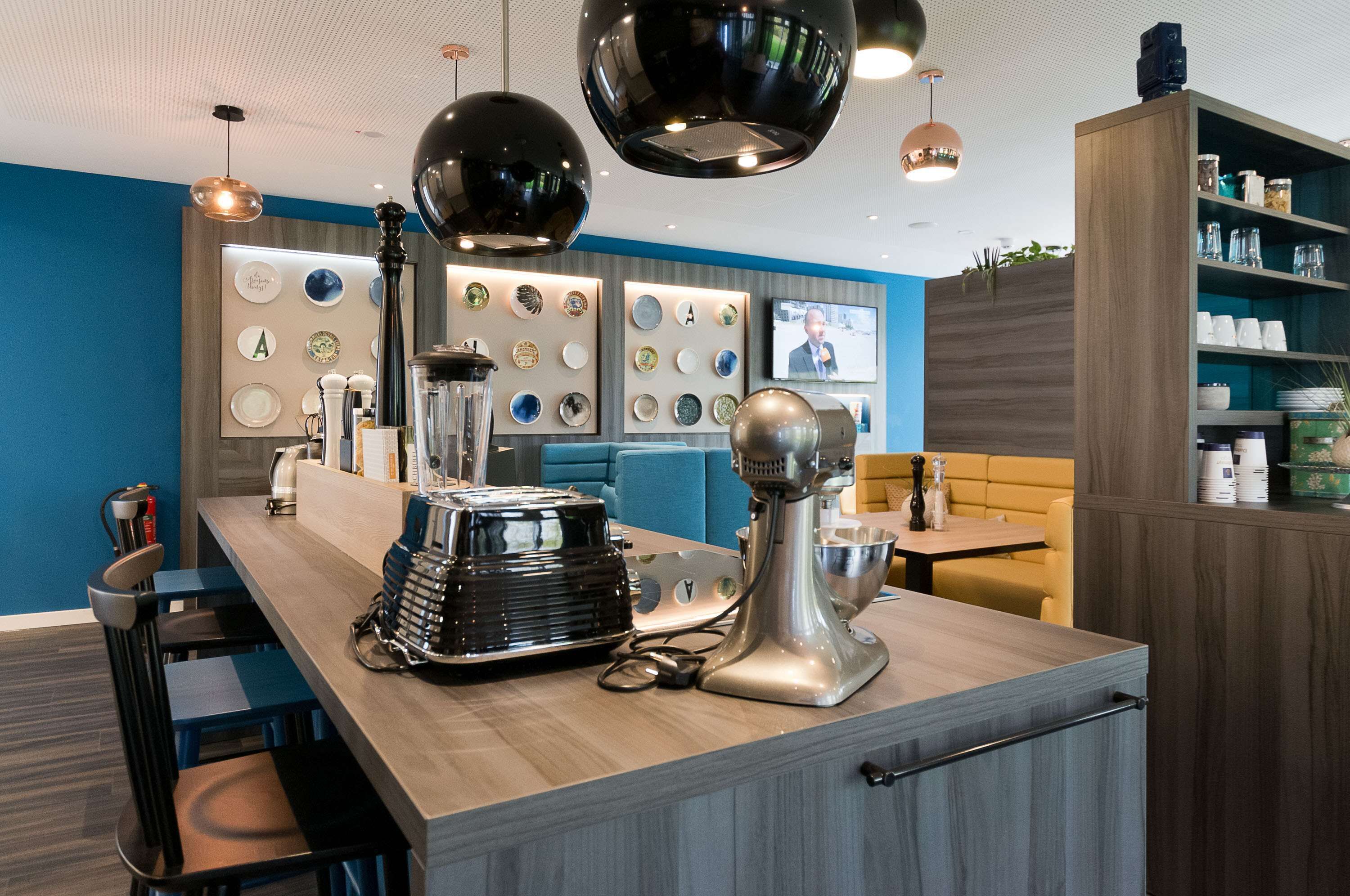 A modern kitchen area with a coffee machine, a mixer, and a display of plates on the wall.