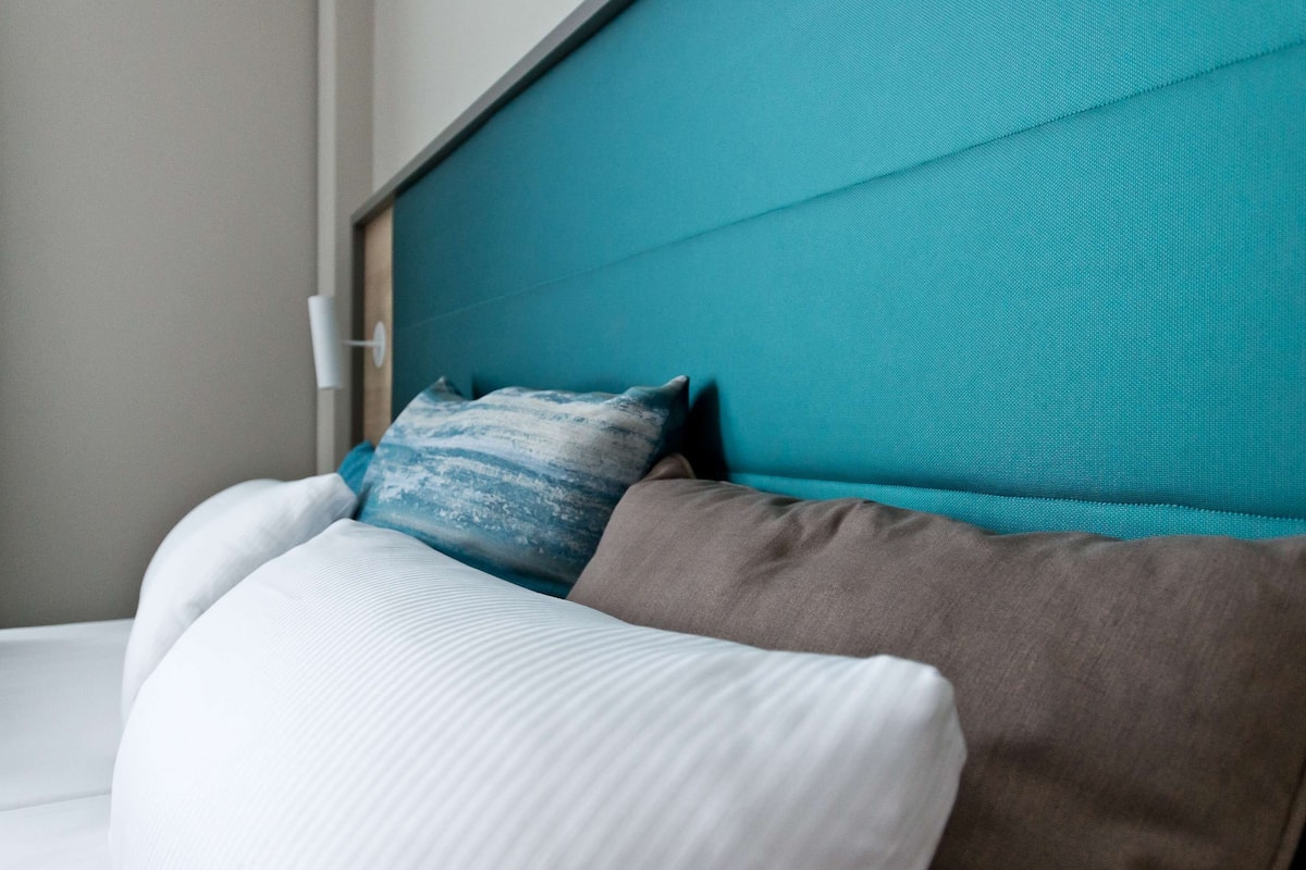 A bed with a teal headboard, white and brown pillows, and a white mattress.