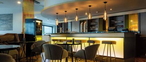Zona de bar moderna con barra curva, taburetes y lámparas colgantes.