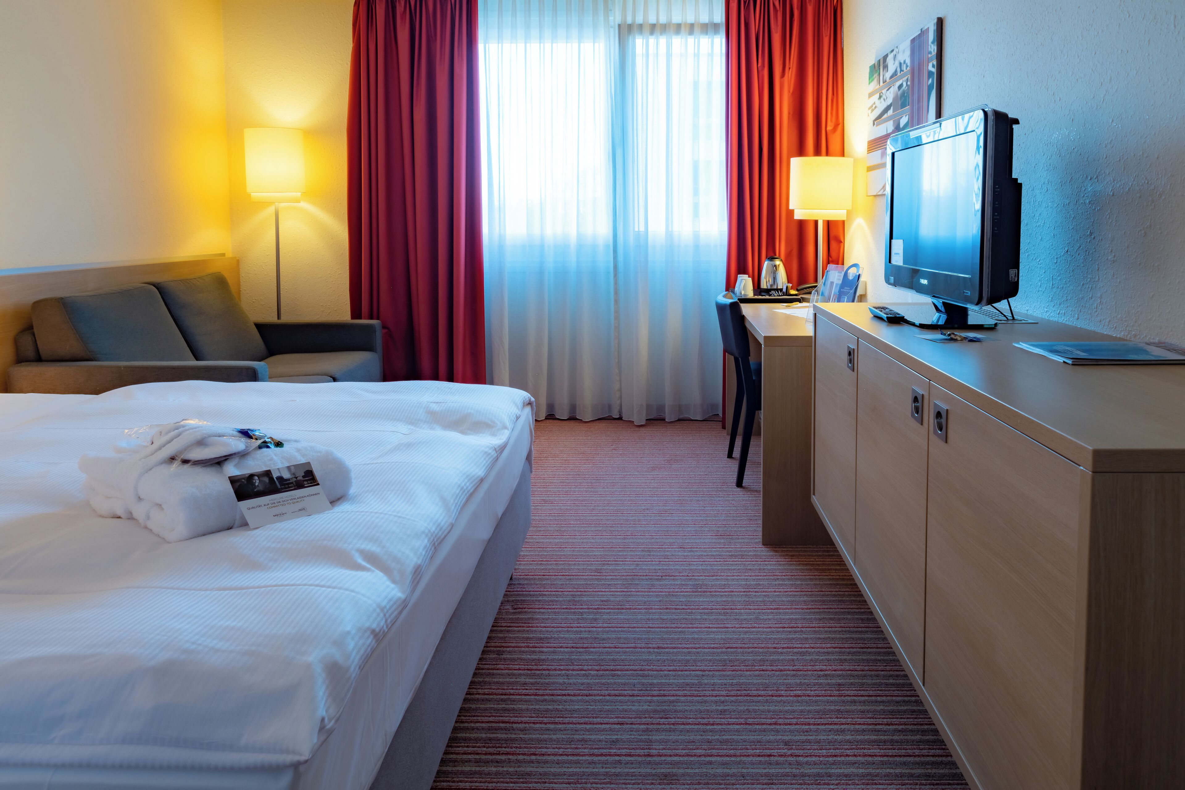 Ein Hotelzimmer mit Bett, Schreibtisch, Fernseher und Lampe.