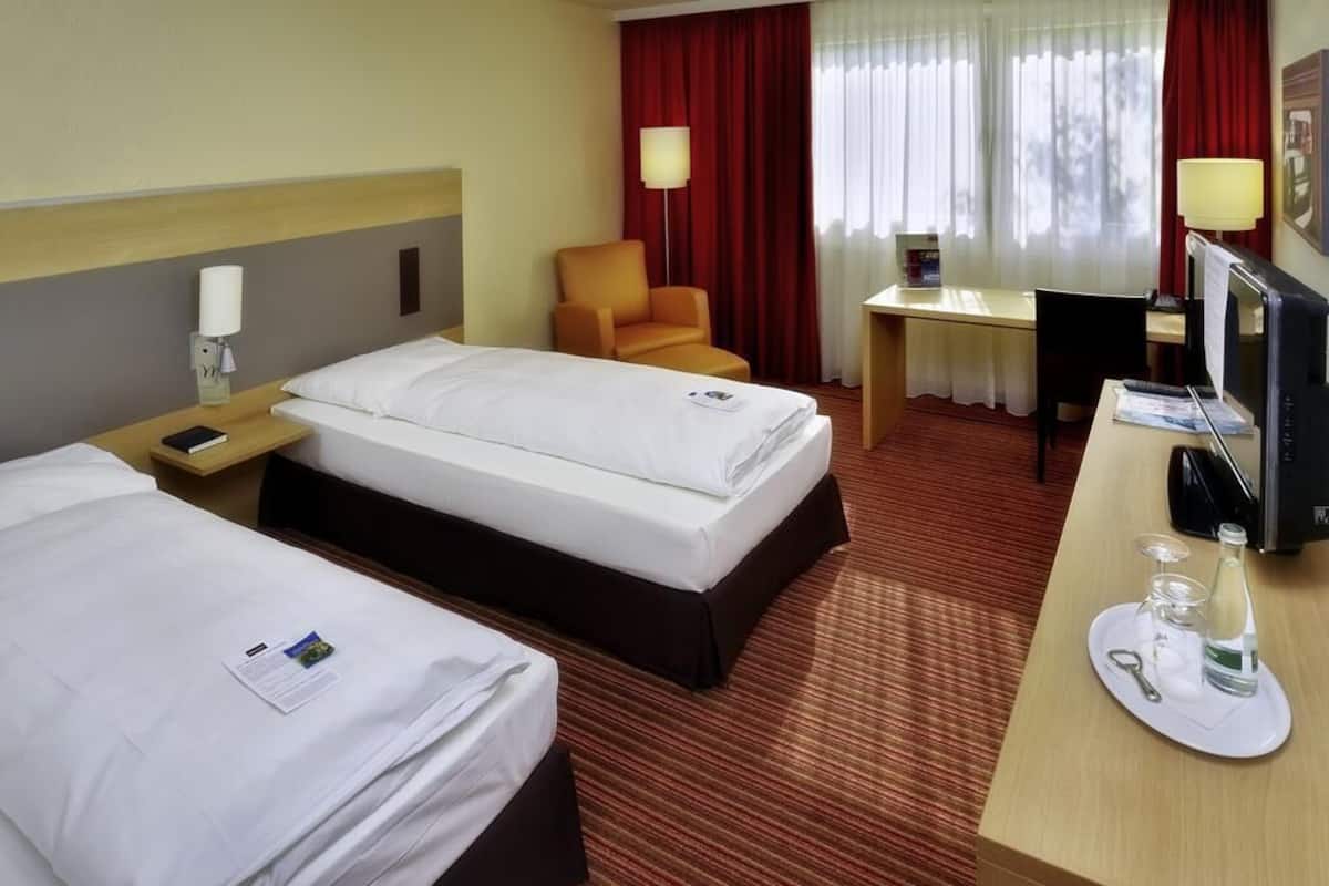 A hotel room with two beds, a desk, a chair, and a TV.
