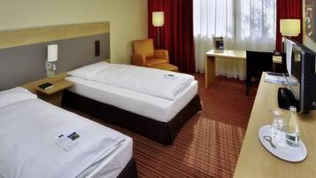 Ein Hotelzimmer mit zwei Betten, einem Schreibtisch, einem Sessel und einem Fernseher.