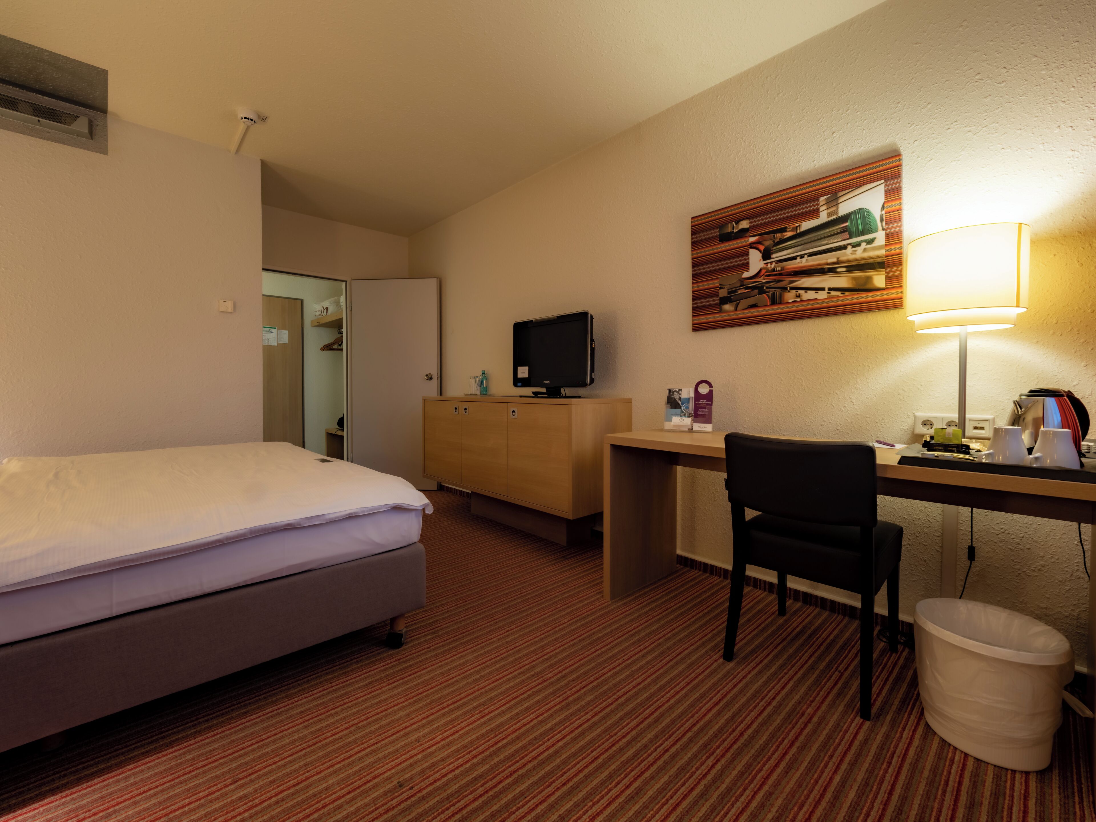 Ein Hotelzimmer mit Bett, Schreibtisch, Stuhl und Mülleimer.