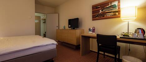 Ein Hotelzimmer mit Bett, Schreibtisch, Stuhl und Mülleimer.