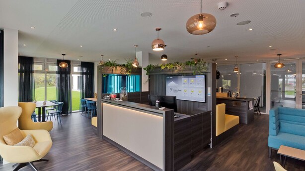A modern hotel lobby with a reception desk, seating areas, and large windows offering a view of the outdoors. - elaya hotel stuttgart boeblingen (Boeblingen)