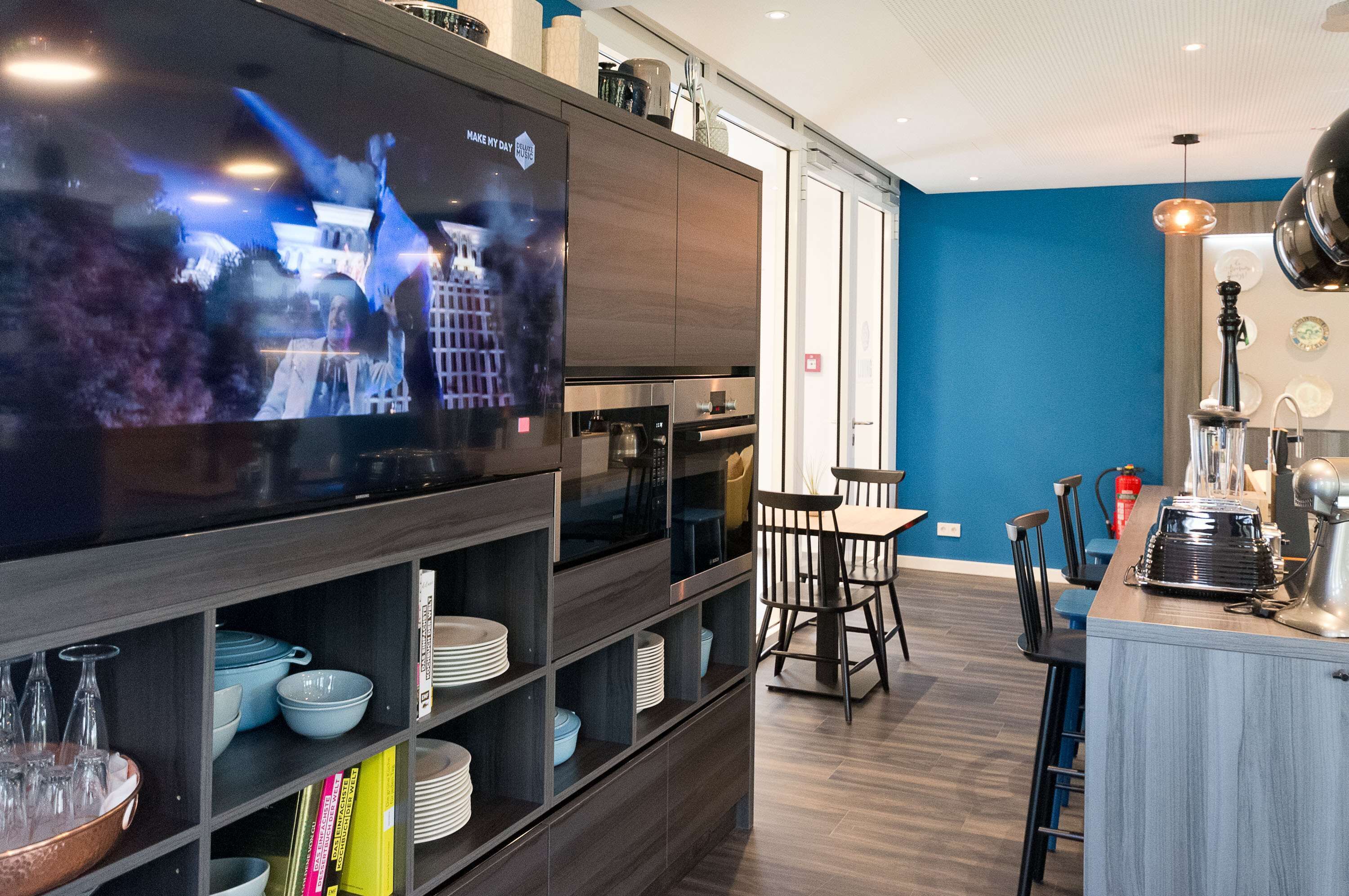 Una cocina moderna con televisor de pantalla plana, gabinetes de madera oscura y una zona de comedor con mesa y sillas.