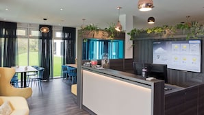A modern hotel lobby with a reception desk, seating area, and a large screen displaying weather information. - elaya hotel stuttgart boeblingen (Boeblingen)