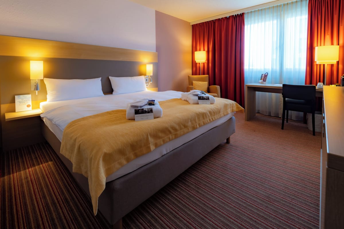 A hotel room with a large bed, two bedside tables, a desk, and a chair.