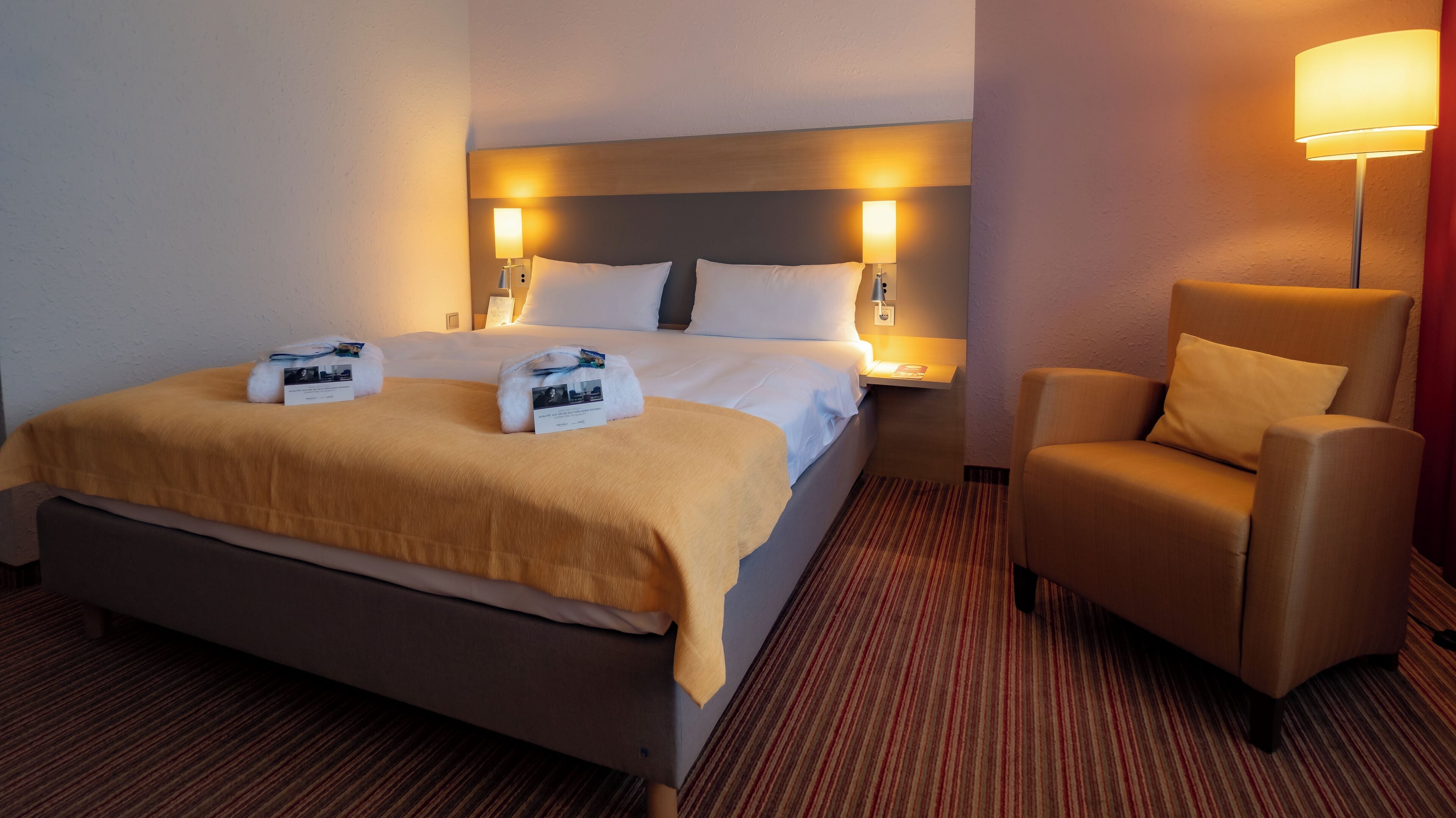 A hotel room with a large bed, two bedside lamps, a chair, and a carpeted floor.