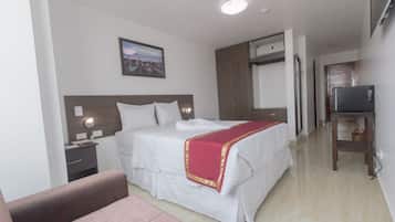 A hotel room with a bed, a nightstand, a television, and a painting on the wall.